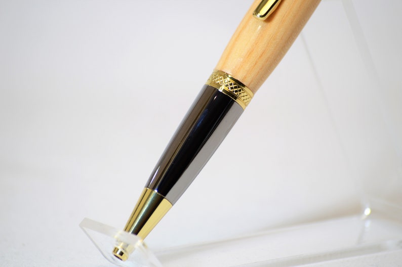 Peut inclure: Gros plan d'un stylo en bois avec des d&eacute;tails dor&eacute;s et argent&eacute;s. Le stylo pr&eacute;sente un corps en bois clair, un corps argent&eacute; et des garnitures dor&eacute;es. Il est pr&eacute;sent&eacute; sur un pr&eacute;sentoir en acrylique transparent.