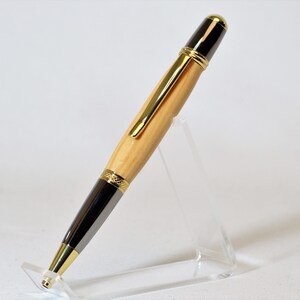 Peut inclure: Un stylo en bois artisanal avec un corps marron clair et des accents gris fonc&eacute;. Le stylo pr&eacute;sente des garnitures dor&eacute;es et un dessus noir. Il est pr&eacute;sent&eacute; sur un pr&eacute;sentoir en acrylique transparent, mettant en valeur son design &eacute;l&eacute;gant et son savoir-faire.