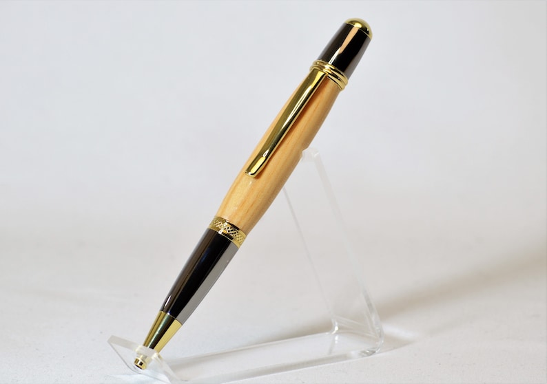Peut inclure: Un stylo en bois artisanal avec un corps marron clair et des accents gris fonc&eacute;. Le stylo pr&eacute;sente des garnitures dor&eacute;es et un dessus noir. Il est pr&eacute;sent&eacute; sur un pr&eacute;sentoir en acrylique transparent, mettant en valeur son design &eacute;l&eacute;gant et son savoir-faire.