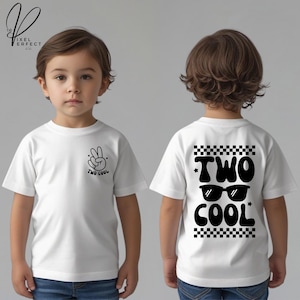 May include: White t-shirt with black graphics. The front features a peace sign and the words "TWO COOL". The back displays "TWO COOL" with sunglasses and a checkered pattern. The shirt is worn by a young child.