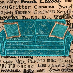 May include: Embroidered turquoise couch with two pillows, each with a brown border. The couch is on a beige background with black text.