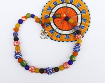 Peut inclure: Un collier de perles colorées avec des perles de verre orange, jaune, bleu, vert et rouge. Il est présenté avec un dessous de verre rond, perlé, orange et blanc avec un motif détaillé. Le collier a un fermoir argenté. Les perles sont mesurées en centimètres.