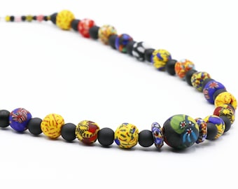 Peut inclure: Un collier de perles coloré avec des perles noires, jaunes, bleues, rouges et vertes. Les perles ont des motifs et des designs complexes.
