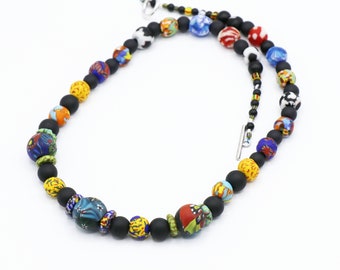Peut inclure: Un collier de perles coloré avec des perles mates noires et des perles de verre aux couleurs vives et aux motifs complexes. Le collier a un fermoir argenté.