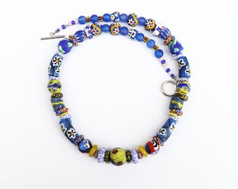 Peut inclure: Un collier de perles bleues et jaunes avec un fermoir argenté. Les perles sont en verre et présentent une variété de motifs.
