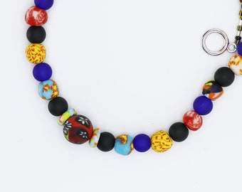 Peut inclure: Un collier de perles colorées avec des perles noires, bleues, jaunes, rouges et blanches. Le collier a un fermoir argenté.