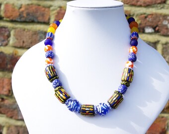 Peut inclure: Un collier coloré composé de perles de verre bleues, orange et jaunes. Les perles sont de formes et de tailles variées, notamment rondes, cylindriques et irrégulières.