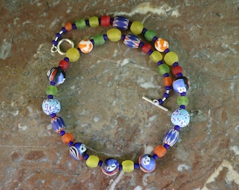 Peut inclure: Un collier coloré composé de perles de verre avec différents motifs et couleurs, notamment bleu, vert, jaune, rouge et orange. Le collier a un fermoir argenté.