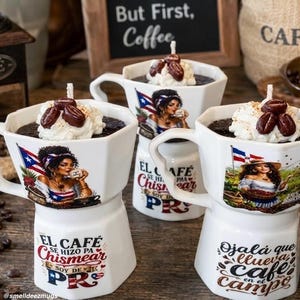 May include: White coffee mugs with a unique design, featuring a woman, a flag, and text. Each mug is filled with a dark liquid, topped with whipped cream and coffee beans. The mugs have a distinctive shape and are decorated with colorful images.