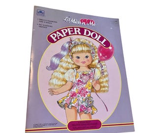 May include: A vintage "Lil Miss 'n Me" paper doll book. The cover features a cartoon illustration of a blonde girl holding a pink balloon. The doll wears a floral dress. The book is purple with text that reads "Paper Doll".