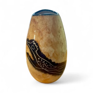 May include: A handcrafted, oval-shaped vase with a textured, tan and brown surface. The vase features a dark blue rim and a stylized, black and white bird design on its side. The design is reminiscent of ancient art.