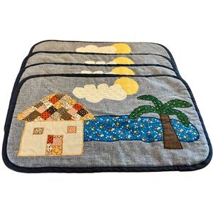 May include: Set of four placemats with a beach scene design. Each placemat features a house, palm tree, sun, clouds, and ocean. The placemats have a blue border and are made of fabric.