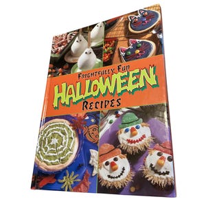 May include: A cookbook titled "Frightfully Fun Halloween Recipes" with an orange cover and various Halloween-themed food images. The images include ghost-shaped treats, cat-shaped cookies, and scarecrow cupcakes. The book is open, displaying colorful food arrangements.