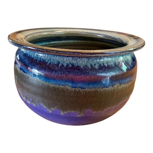 May include: A round ceramic bowl with a wide, flat rim. The exterior features a layered glaze with a deep purple base, a dark brown middle section, and a vibrant blue upper band that transitions into a light, creamy white edge at the top rim.