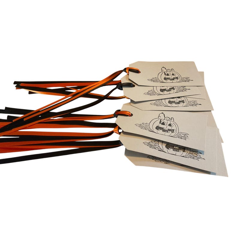 May include: A stack of beige gift tags with a black jack-o'-lantern design. Each tag has orange and black ribbons attached. The tags are for Halloween or fall-themed gifts.