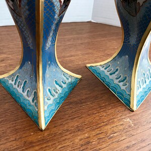 May include: Two blue and gold cloisonn&eacute; vases with a wave pattern and floral designs. The vases are made of metal and have a square base.