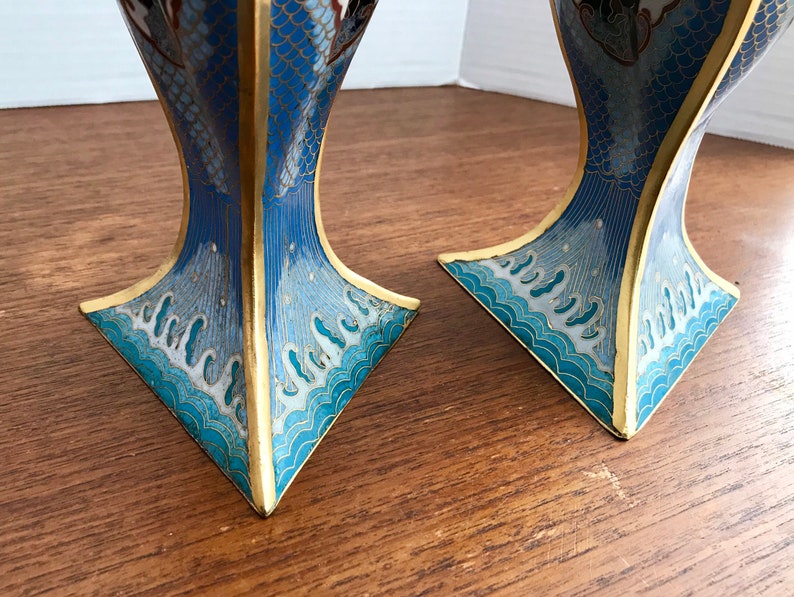 May include: Two blue and gold cloisonn&eacute; vases with a wave pattern and floral designs. The vases are made of metal and have a square base.