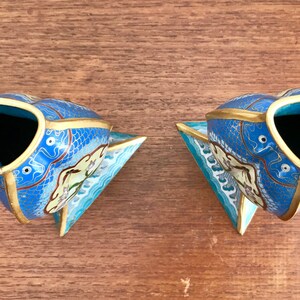 May include: A pair of blue and gold cloisonn&eacute; vases shaped like fish. The vases have a white and blue floral design and are decorated with gold accents.