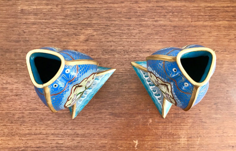 May include: A pair of blue and gold cloisonn&eacute; vases shaped like fish. The vases have a white and blue floral design and are decorated with gold accents.