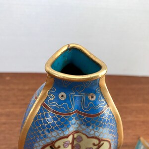 May include: A pair of blue and gold cloisonn&eacute; vases shaped like fish. The vases have intricate designs of scales, flowers, and clouds. The vases are made of enamel and metal.