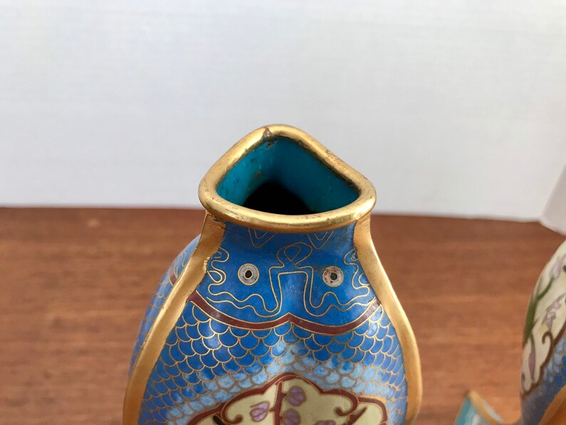 May include: A pair of blue and gold cloisonn&eacute; vases shaped like fish. The vases have intricate designs of scales, flowers, and clouds. The vases are made of enamel and metal.