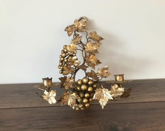 May include: Gold metal wall sconce with a grapevine design and three candle holders. The sconce is decorated with gold leaves and grapes.