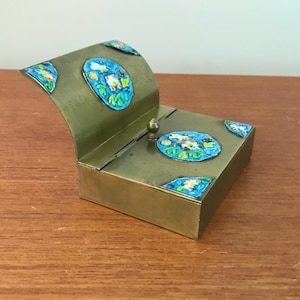 Peut inclure: Une boîte en laiton avec un couvercle à charnière décoré d'émail bleu et vert. La boîte a un motif floral et est fermée.