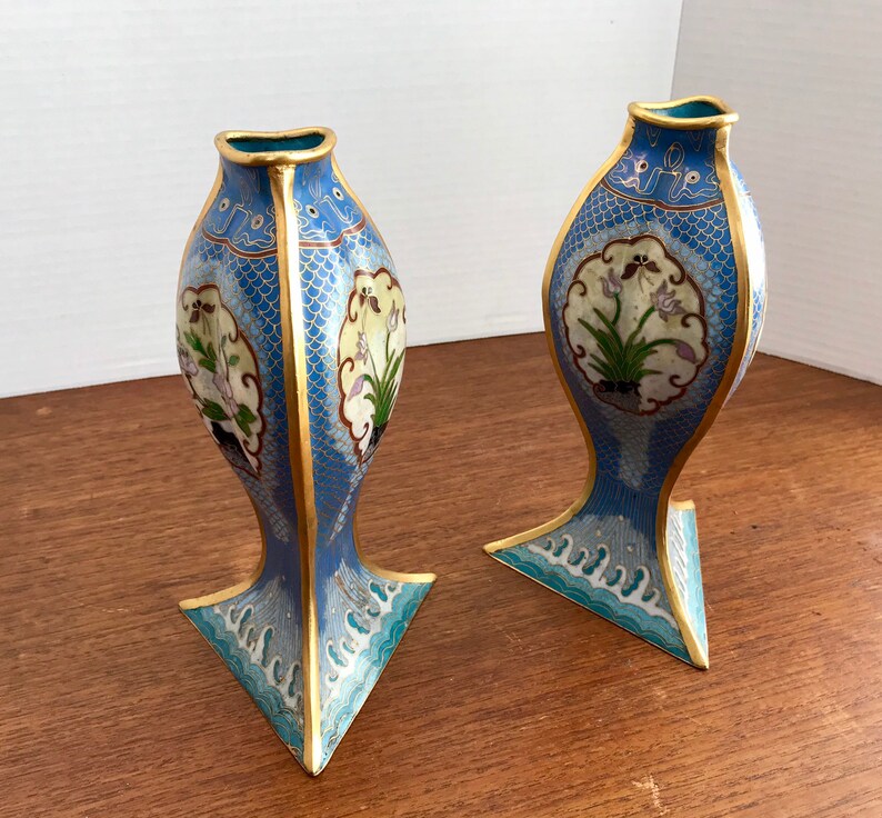 May include: A pair of blue and gold cloisonn&eacute; vases with floral designs. The vases are shaped like fish and have a triangular base.