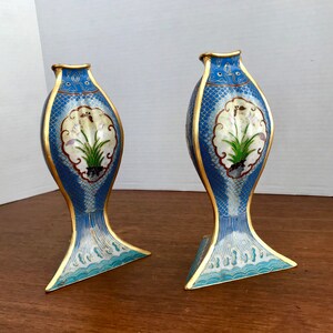 May include: A pair of blue and white cloisonn&eacute; vases with gold accents. The vases are shaped like fish and feature a floral design.