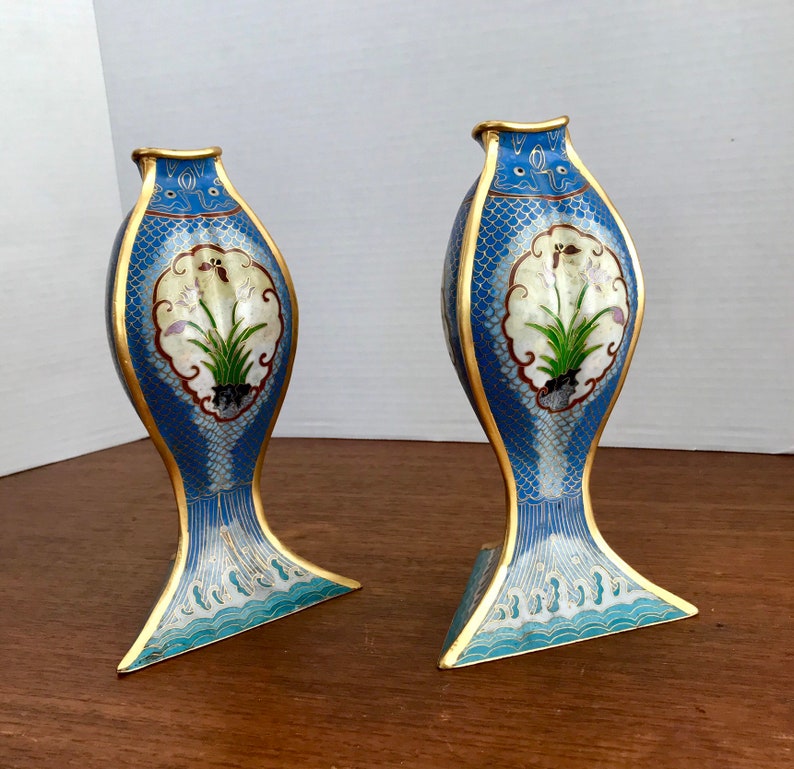 May include: A pair of blue and white cloisonn&eacute; vases with gold accents. The vases are shaped like fish and feature a floral design.