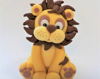 May include: A yellow and brown fondant lion cake topper with a brown mane, brown eyes, and pink paw pads.