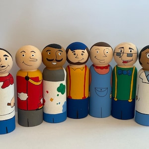 May include: A set of seven hand-painted wooden peg dolls featuring diverse characters. The figures include a chef, a red-coated guard, an artist with paint splatters, a person in yellow suspenders, a person in blue overalls, a person in a green shirt, and a doctor.