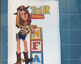 Puede incluir: Una pegatina con un Woody de dibujos animados de Toy Story, con un sombrero de vaquero y sosteniendo un lazo. La pegatina dice "Tour Story" y tiene una pila de bloques de letras que deletrean "NFA" en rojo, amarillo y azul.