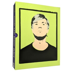 Puede incluir: Un libro verde con el título "Pop Up Pop Art" y una imagen emergente de Andy Warhol. La imagen es un primer plano de la cara de Warhol con un fondo blanco y negro.