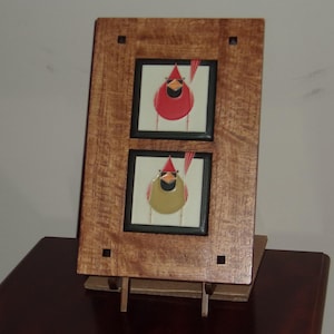 May include: A wooden frame with two square images of red and yellow birds with black eyes and beaks. The frame is on a wooden easel.