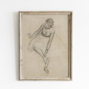 May include: A framed black and white pencil drawing of a ballerina in a tutu, sitting and tying her shoe.