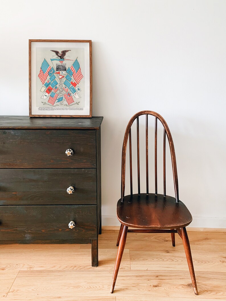 May include: A dark wood dresser with three drawers and black knobs. A wooden chair with a curved back and a wooden seat sits to the right of the dresser. A framed print of an eagle with American flags hangs on the wall above the dresser.
