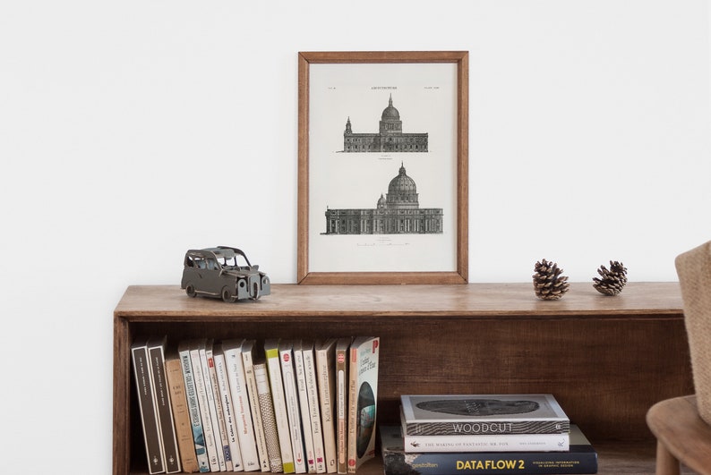 Peut inclure: Une estampe en noir et blanc encadr&eacute;e d'un dessin architectural d'un b&acirc;timent avec un d&ocirc;me. L'estampe est sur une &eacute;tag&egrave;re en bois avec une petite voiture jouet, des livres et des pommes de pin.