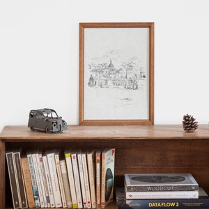 May include: A wooden shelf with a framed black and white drawing of a city scene, a small toy car, and two pine cones. The shelf is filled with books, including "WOODCUT" and "DATA FLOW 2".