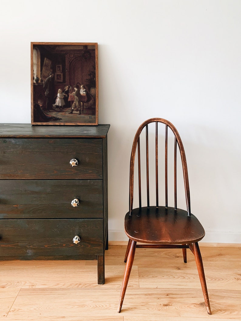 May include: A dark wood dresser with three drawers and black knobs. A framed picture of a group of children in a room hangs above the dresser. A wooden chair with a curved back and a dark wood finish sits to the right of the dresser.