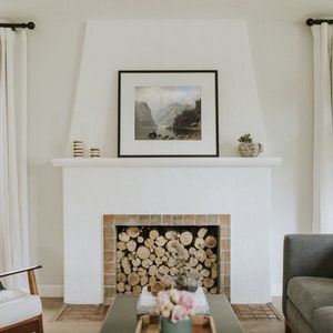 May include: A white fireplace with a brick surround and a wood-burning fire. The fireplace is in a living room with a gray sofa, a white armchair, and a coffee table with a vase of flowers.