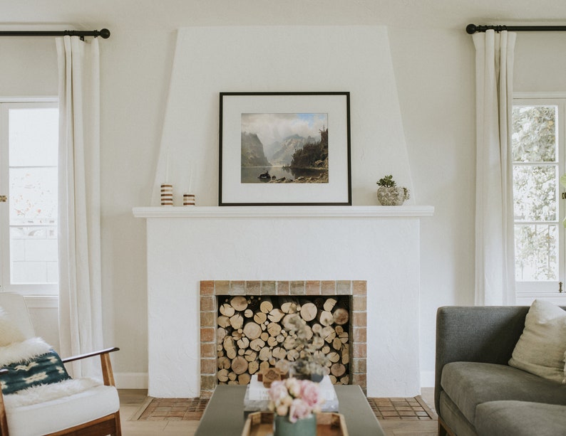 May include: A white fireplace with a brick surround and a wood-burning fire. The fireplace is in a living room with a gray sofa, a white armchair, and a coffee table with a vase of flowers.