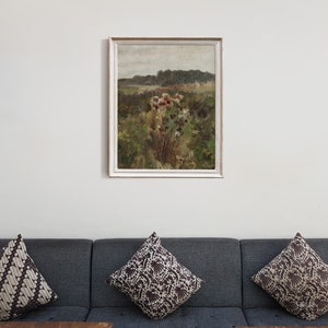 May include: A framed painting of a landscape with a field of wildflowers in the foreground and a forest in the background. The painting is in a white frame and is hanging on a white wall.