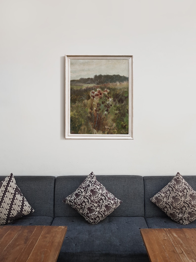 May include: A framed painting of a landscape with a field of wildflowers in the foreground and a forest in the background. The painting is in a white frame and is hanging on a white wall.