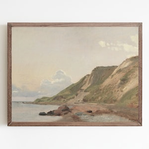 May include: A framed painting of a seascape with a rocky coastline and green hills. The sky is a pale blue with white clouds.