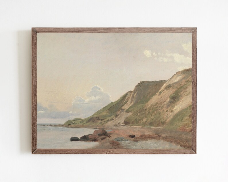 May include: A framed painting of a seascape with a rocky coastline and green hills. The sky is a pale blue with white clouds.