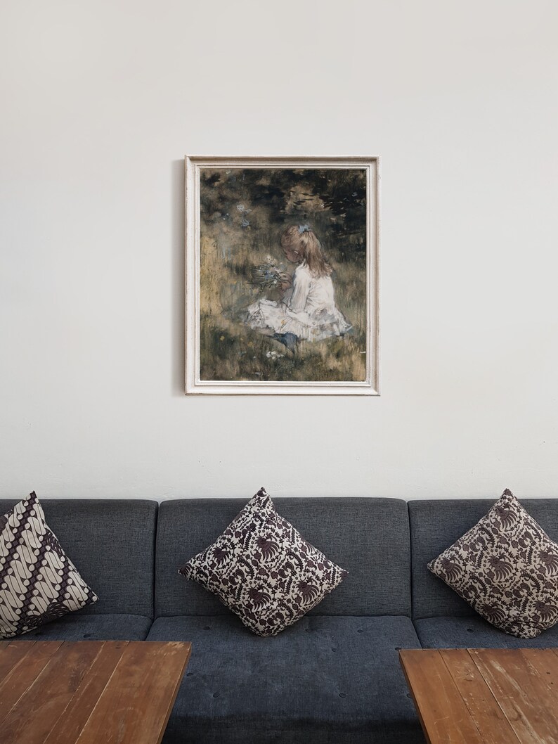 May include: A framed painting of a young girl in a white dress sitting in a field of flowers. The painting is done in a watercolor style and has a soft, dreamy feel.