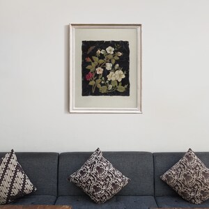 以下が含まれることがあります： 黒い背景に白い花とピンクの花がアレンジされた額装されたアート作品。花は房状に配置されており、押し花のように見える。
