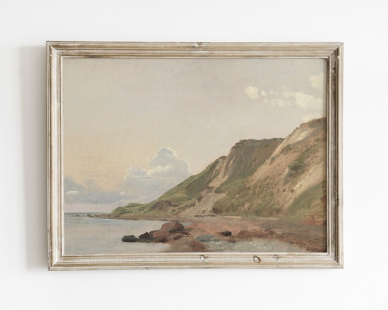May include: A framed painting depicting a seascape with a rocky coastline and green hills. The sky is a soft blue with white clouds. The water is a calm blue with a hint of green.