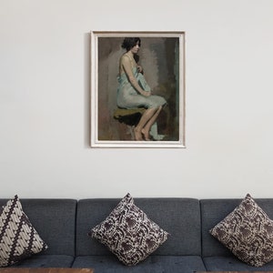May include: A framed painting of a woman in a light blue dress sitting on a stool. The woman is looking to the side and has dark hair. The painting is set against a white wall.